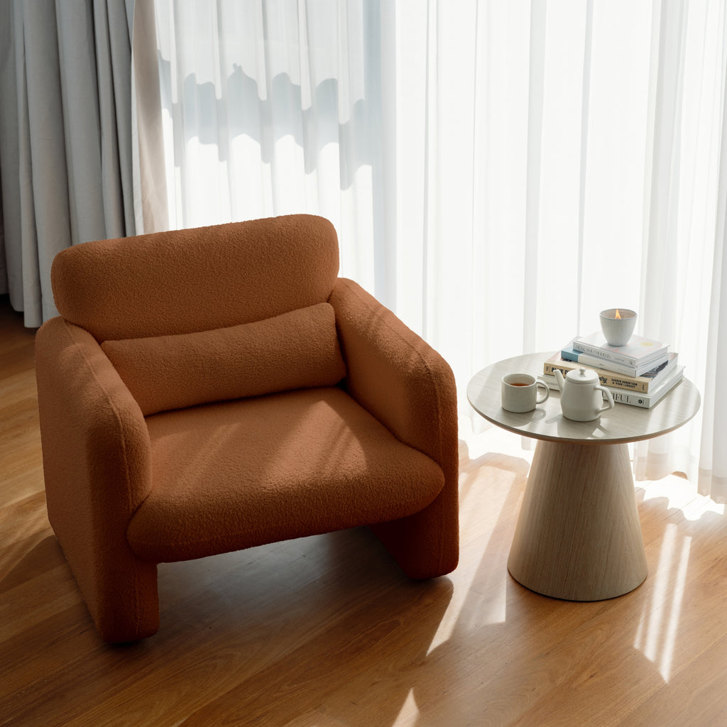 An image featuring an amber-coloured armchair with a minimalist design in a room with a side table