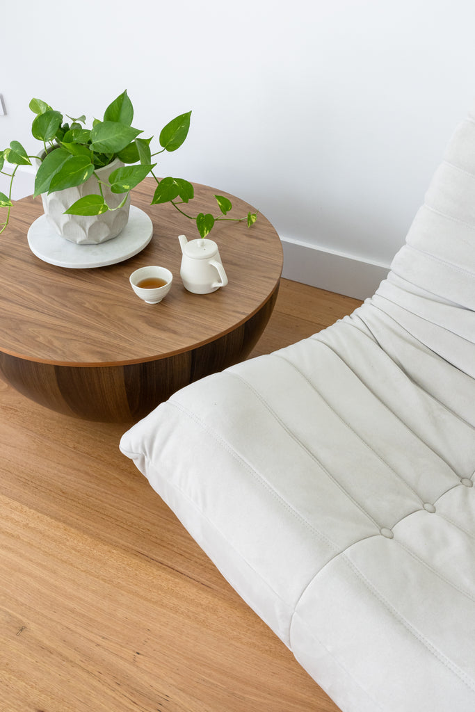 A round, chestnut coffee table with a vase and tea set on top.
