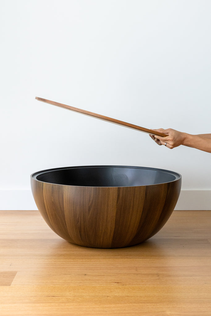 A round, chestnut coffee table with a smooth finish, placed on a wooden floor with an open top.