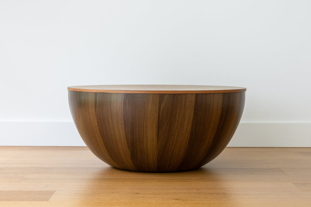 A round, brown walnut veneer coffee table with a smooth finish, placed on a wooden floor against a white background.