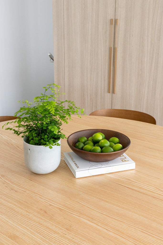 A round wooden dining table top view with  a vase, a book, and bowl of fruits