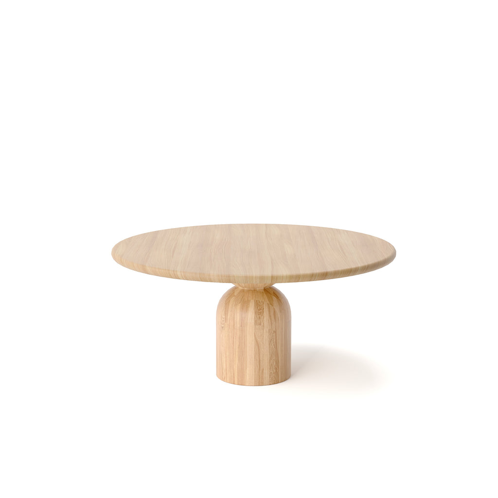 A round, natural wood finish dining table in a white wall background