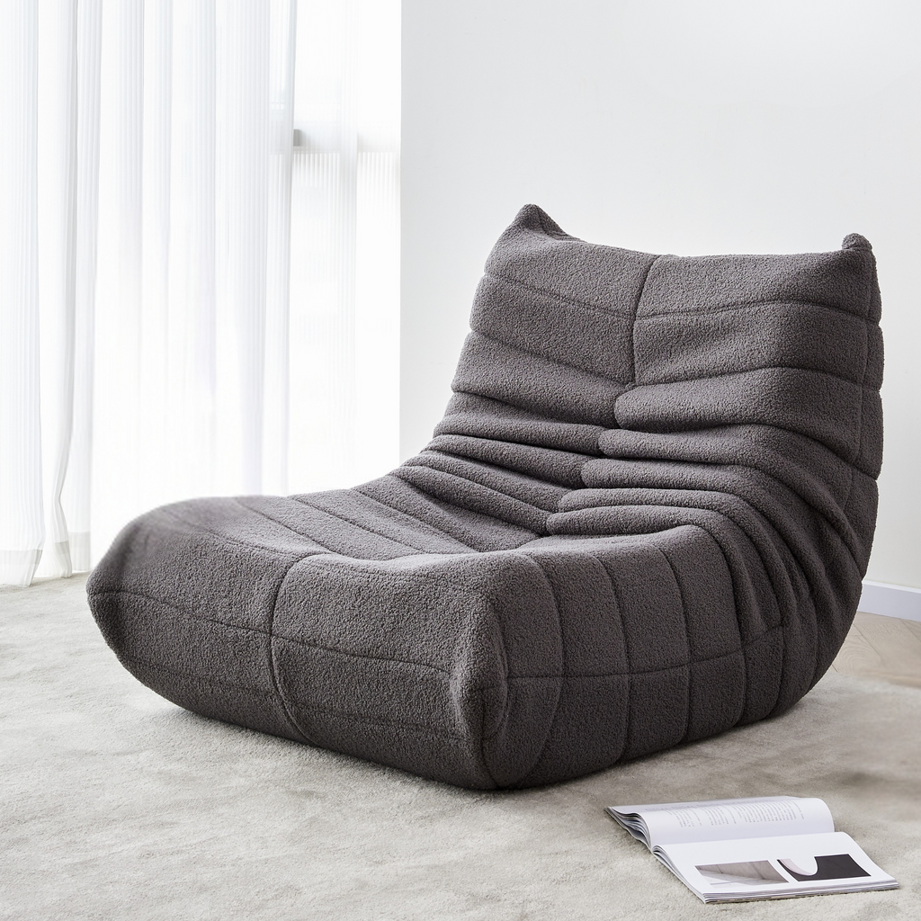 A slate grey, curved single sofa with a relaxed and cushioned appearance, upholstered in synthetic lambswool fabric on the carpet.