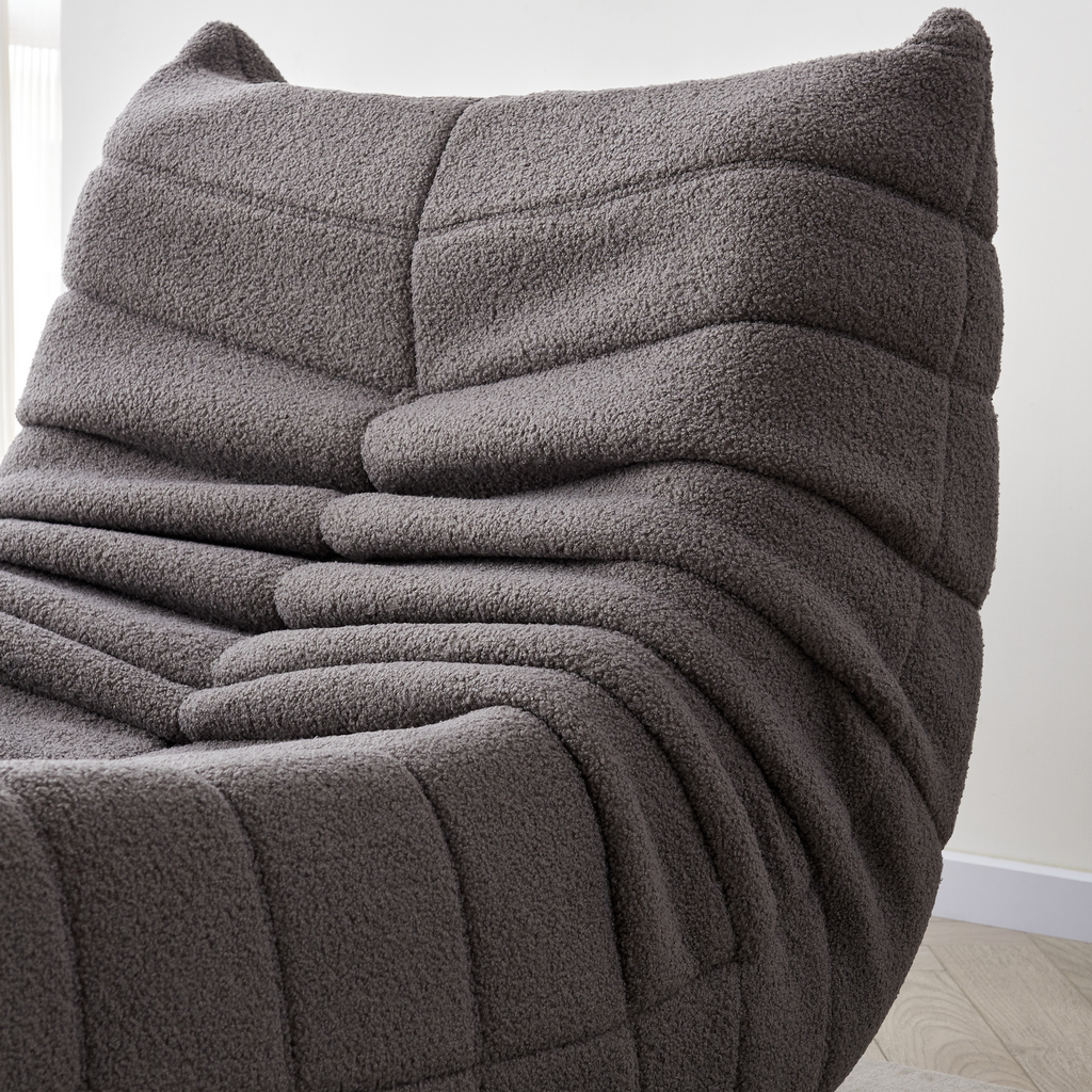 A close-up slate grey, curved single sofa with a relaxed and cushioned appearance, upholstered in synthetic lambswool fabric.