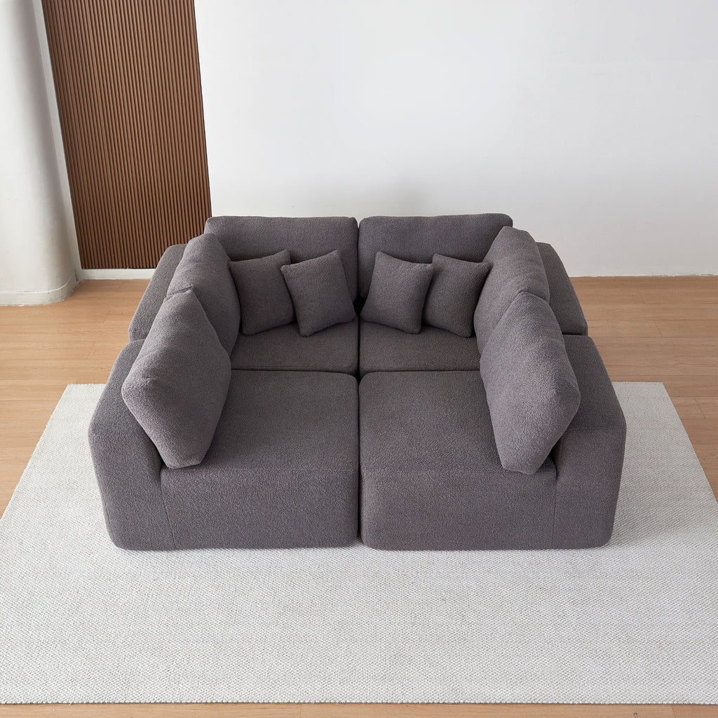 Grey sectional sofa on a white rug with a wooden floor and wall in the background