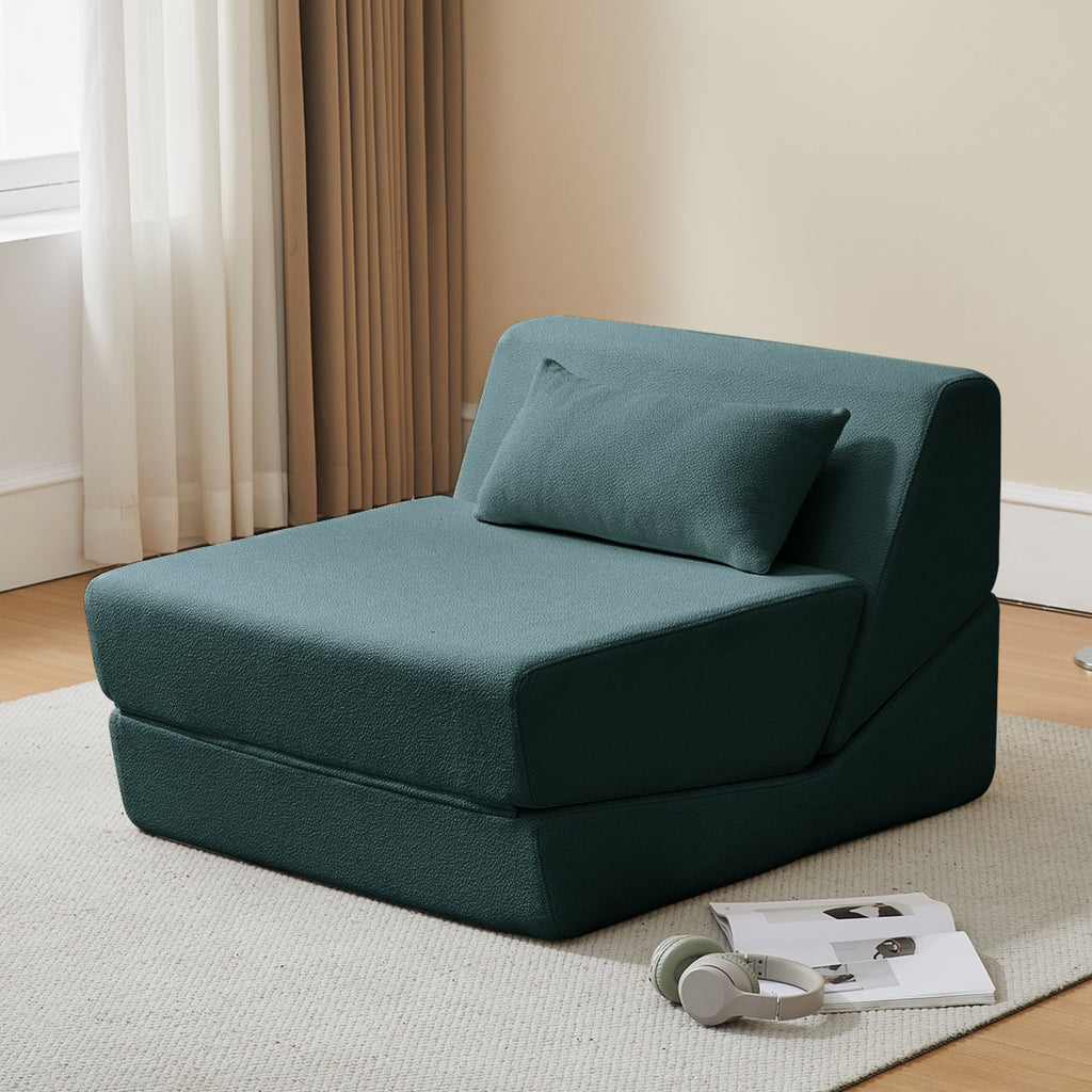 Dark teal wedge-shaped sofa bed in a room with curtains and a rug.