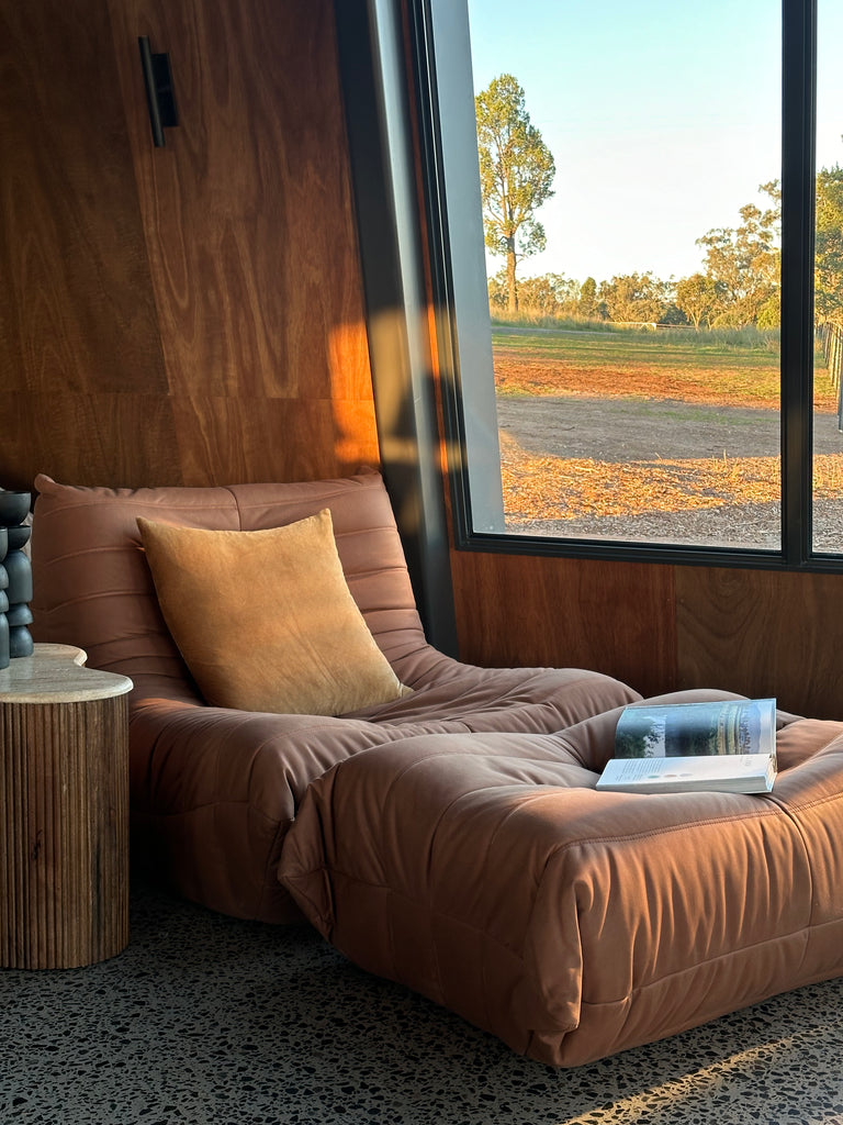 An ochre-coloured Junii Fireside sofa with a unique mid-century modern design at the Glay Estate near the big window.