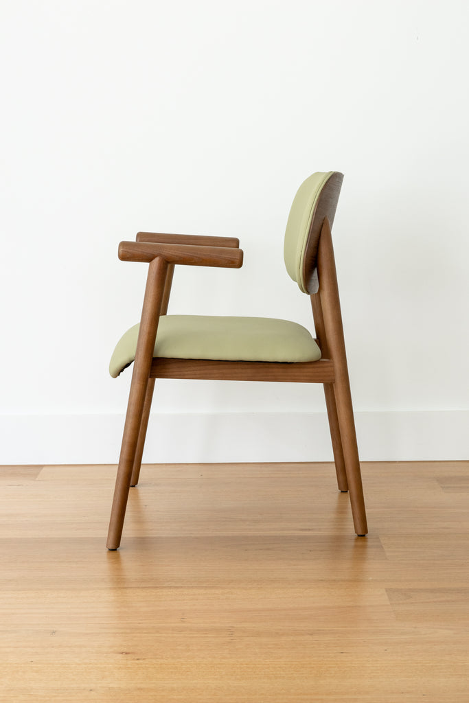 A side view of Kyoto Dining Chair with a green cushioned seat and backrest on a wooden floor.