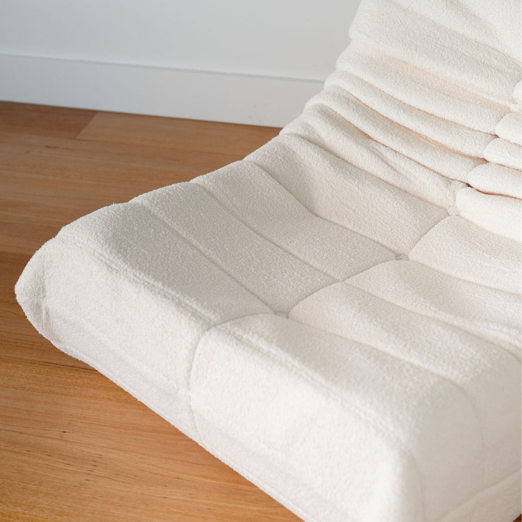 A cream-colored single sofa featuring a curved silhouette and synthetic lambswool upholstery.