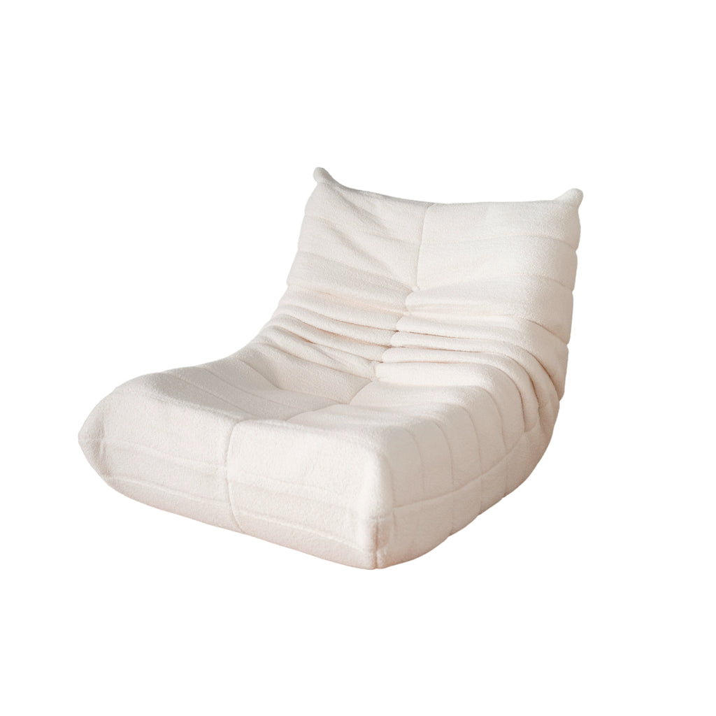 A cream-coloured, single sofa with a relaxed, low-profile design, featuring a curved silhouette and synthetic lambswool upholstery.