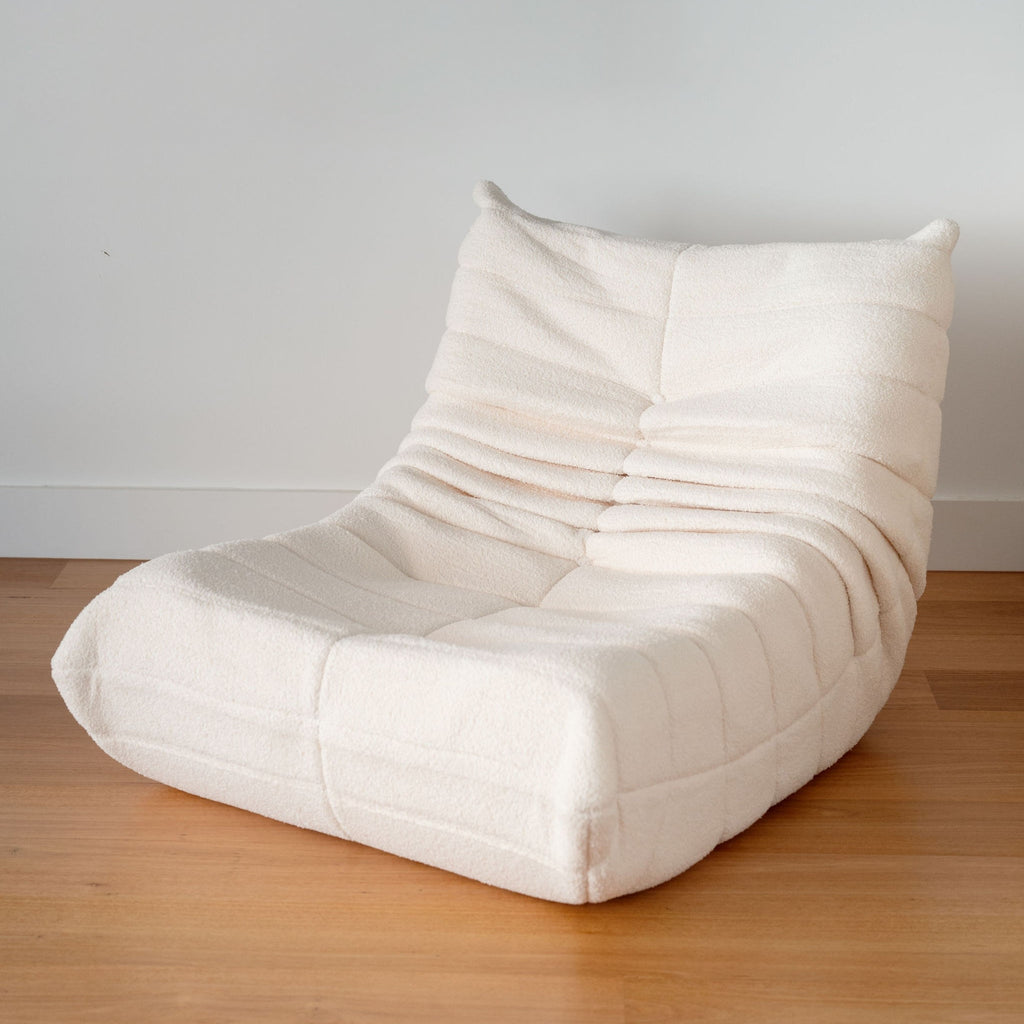A cream-colored, single sofa with a relaxed, low-profile design on a wooden floor