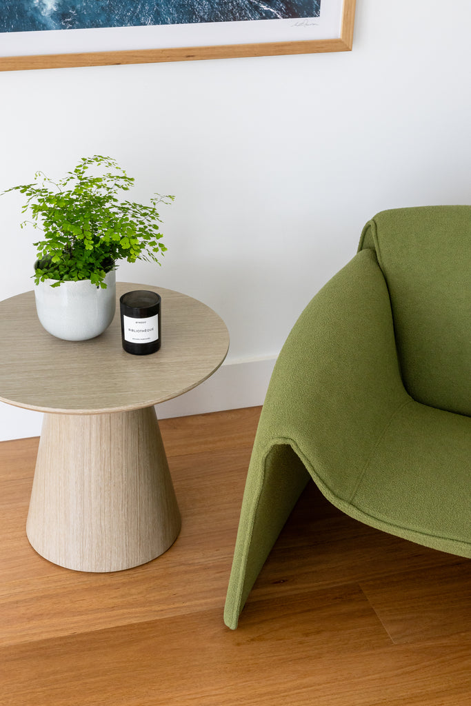 A Naomi Armchair in moss on a wooden floor near the side table.