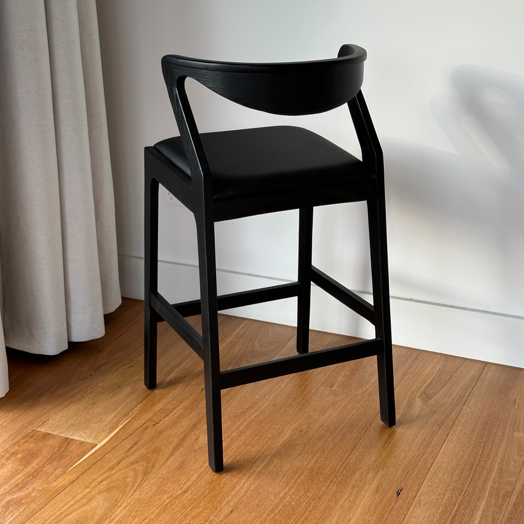 Black bar stool with a modern design on a white background and wooden floor