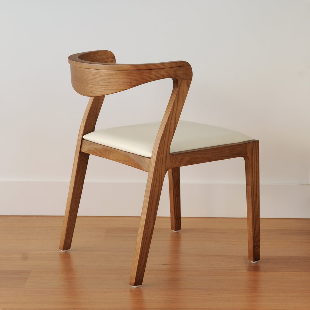 Wooden chair with a white cushion on a wooden floor and light-coloured wall background