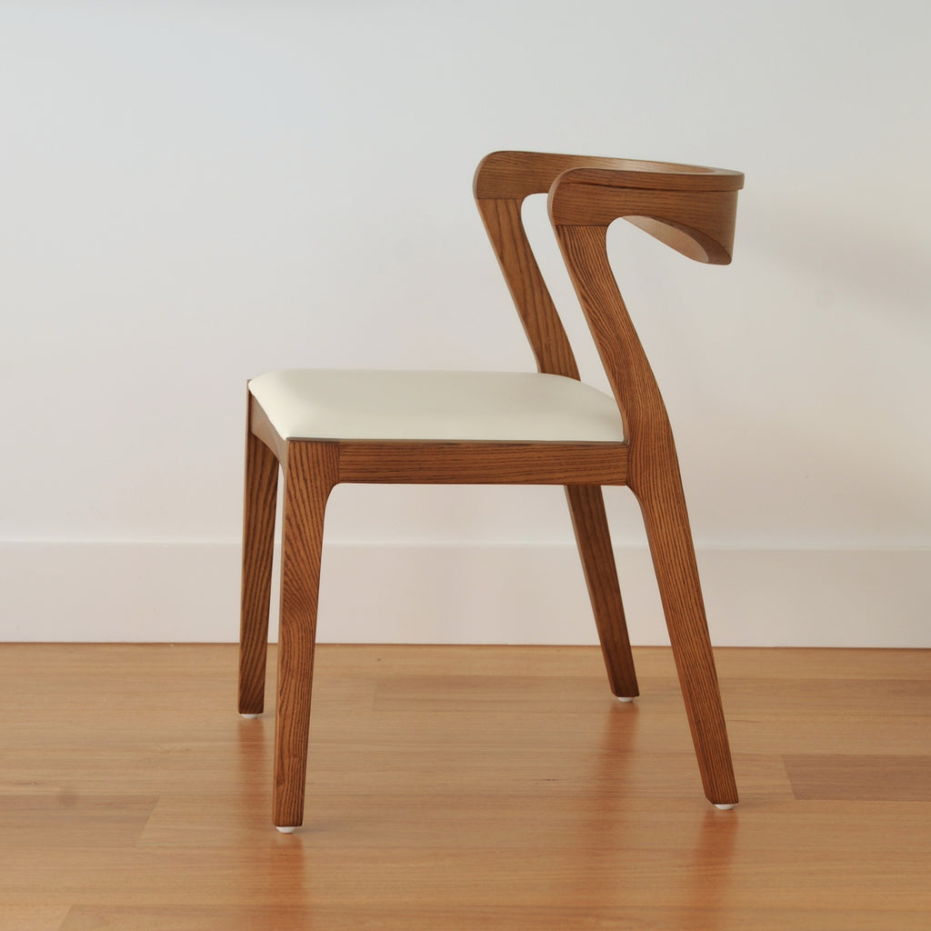Wooden chair with a white cushion on a wooden floor and light-coloured wall background